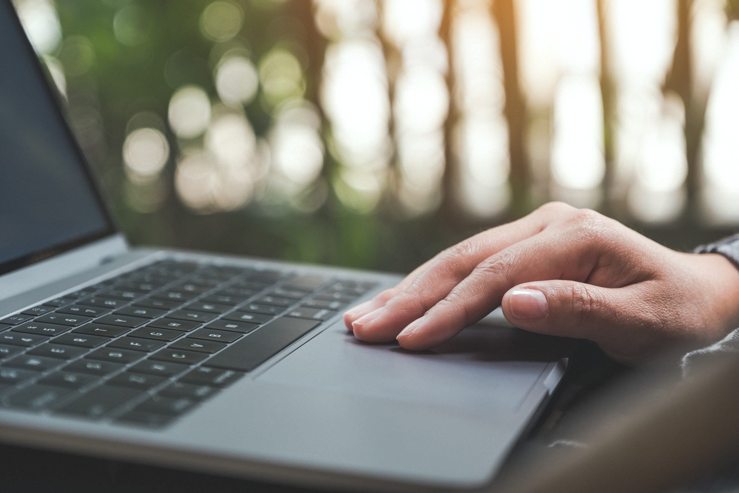 Keene Marketing Agency Close-up of a person's hand resting on a laptop trackpad with a natural, blurry background.
