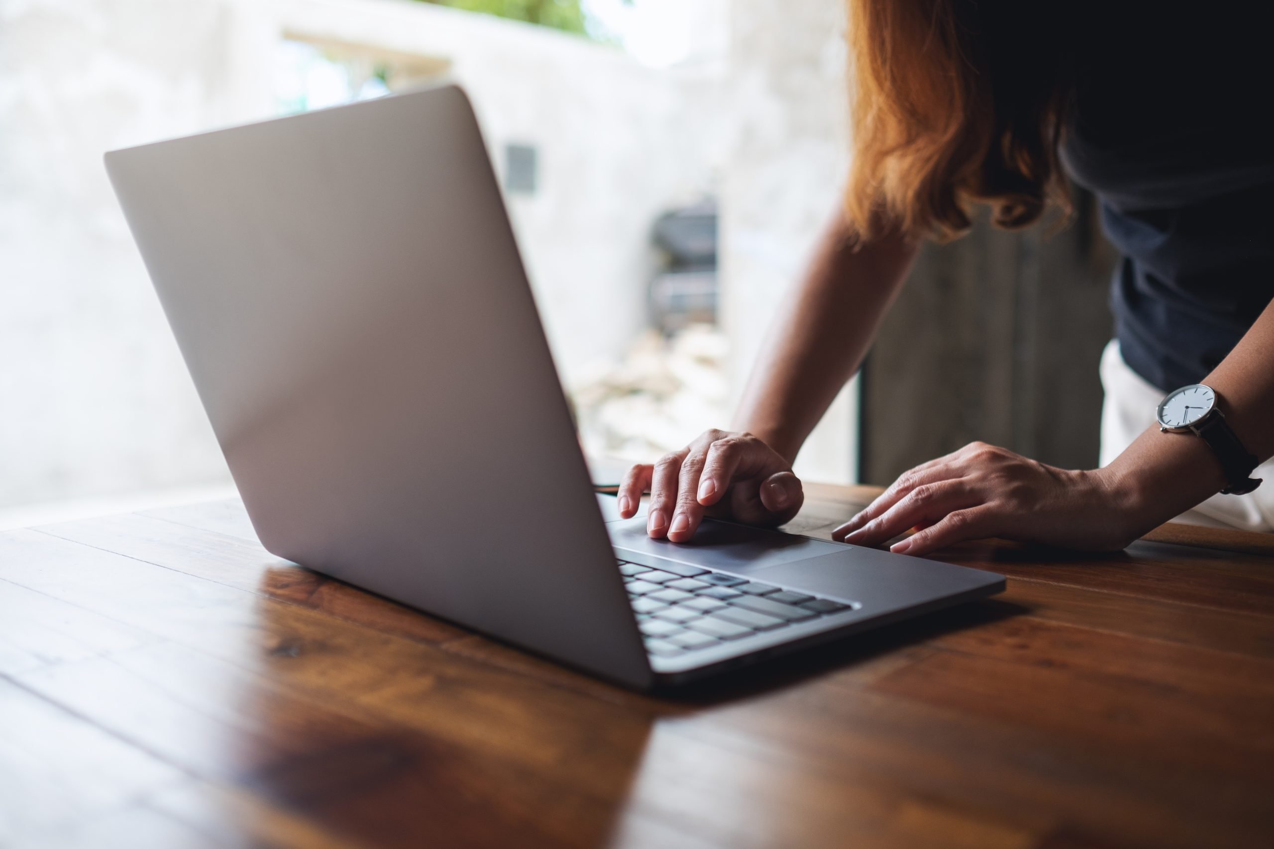 Keene Marketing Agency A person working on a laptop at a wooden table, focusing on the laptop screen, with a blurred background.