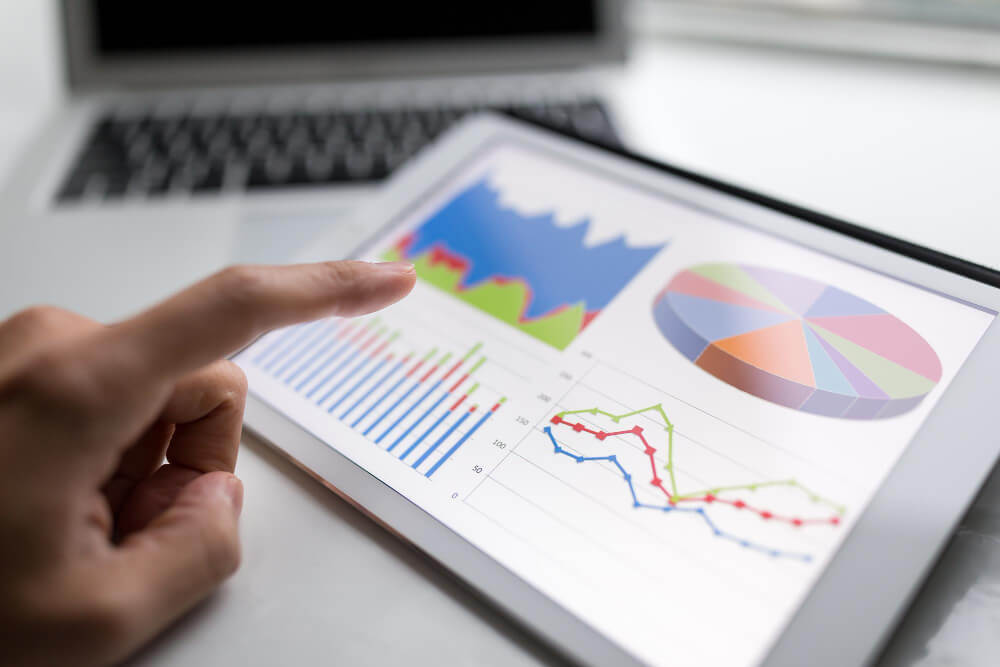 New Hampshire A person in a marketing role is using a tablet displaying various charts and graphs, including a pie chart, line graphs, and bar charts, in front of an open laptop. Marketing Agency