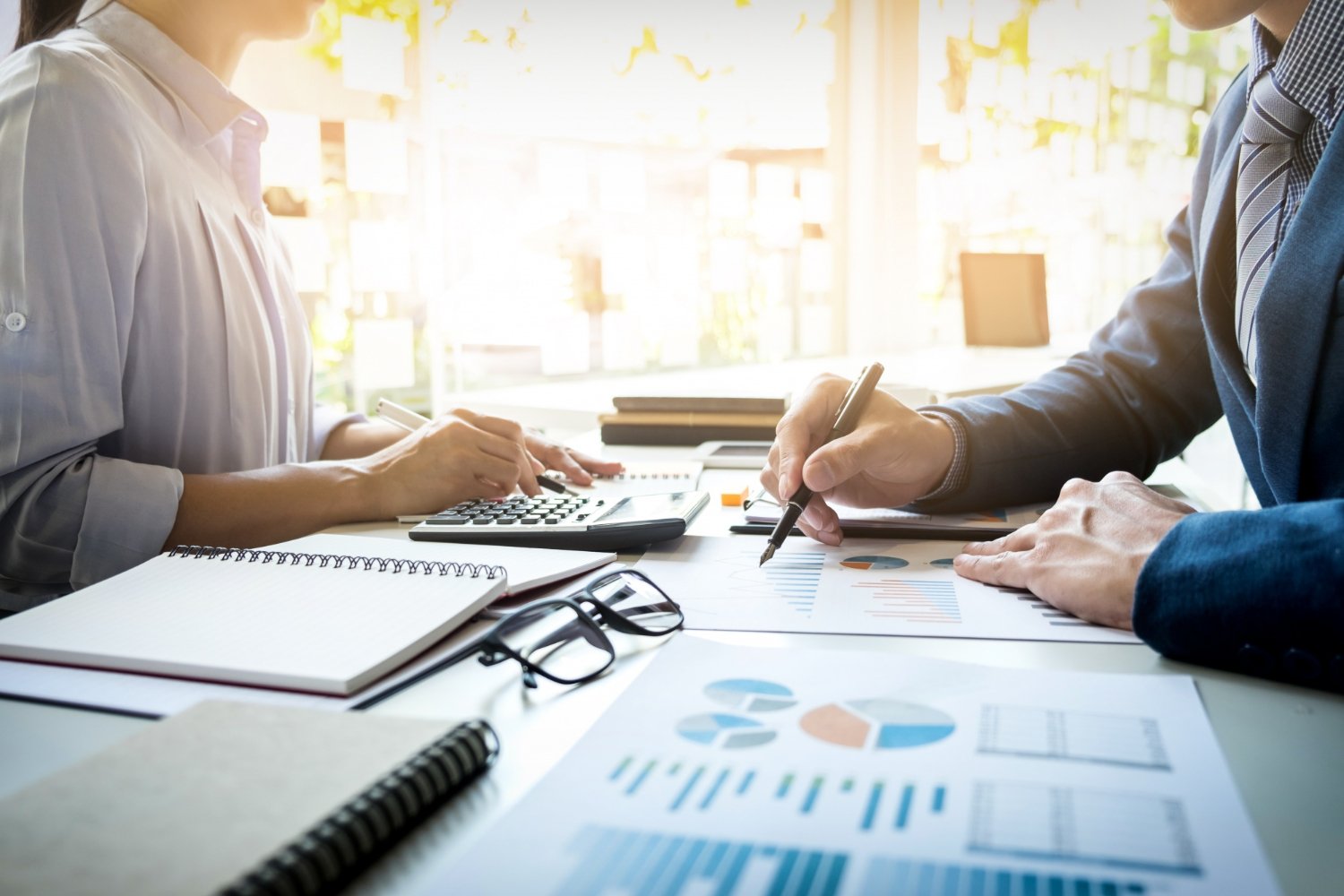 New Hampshire Two people working at a desk with charts, documents, a calculator, and notebooks. One person writes on paper while the other uses a calculator. A pair of glasses lies on the desk as they strategize paid ad campaigns for local businesses.
 Marketing Agency
