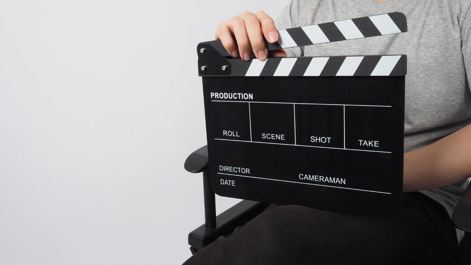 New Hampshire Person holding a black and white clapboard against a plain white background. The clapboard, essential for professional production, has sections labeled for production, roll, scene, shot, take, director, cameraman, and date—key elements in optimizing your video marketing ROI. Marketing Agency
