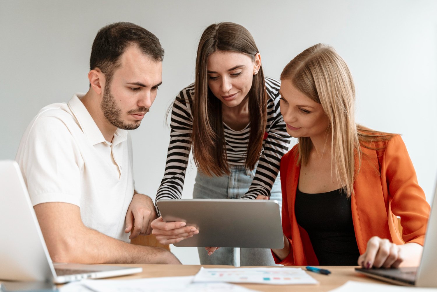 New Hampshire Three people are gathered around a tablet, working together at a desk. The person in the middle is holding the tablet, likely presenting ideas about brand identity to the two others. Laptops and documents related to their home service business are spread out on the desk. Marketing Agency