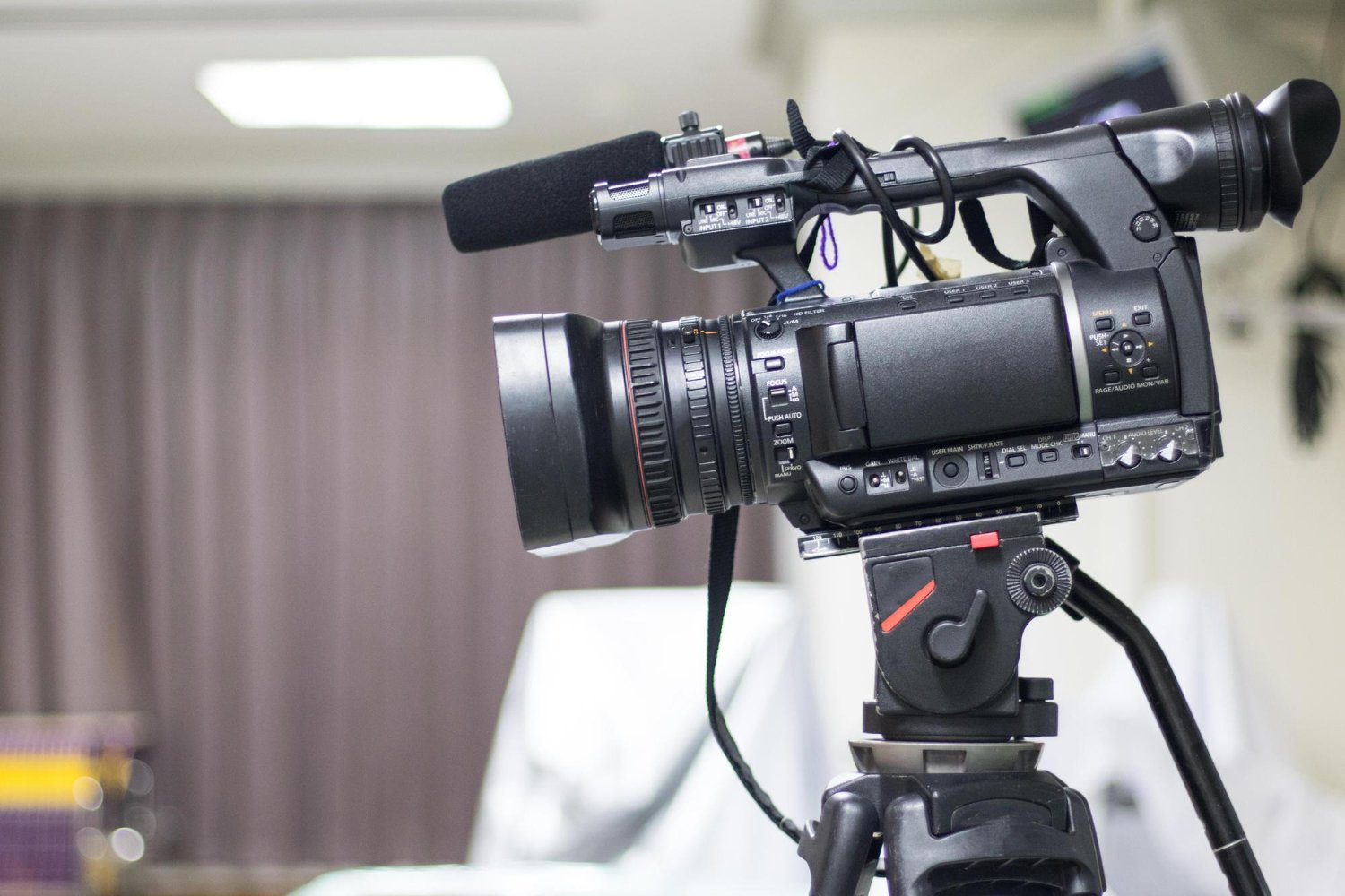 New Hampshire Close-up of a professional video camera on a tripod in a room with a blurred background and curtains, perfect for filming video testimonials to boost business in Keene. Marketing Agency