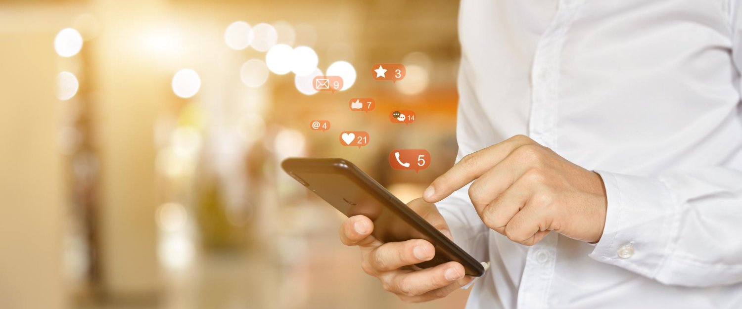 New Hampshire A person wearing a white shirt holds a smartphone, with social media notification icons hovering above the screen, indicating new likes, messages, and comments—a glimpse into the future of marketing. Marketing Agency