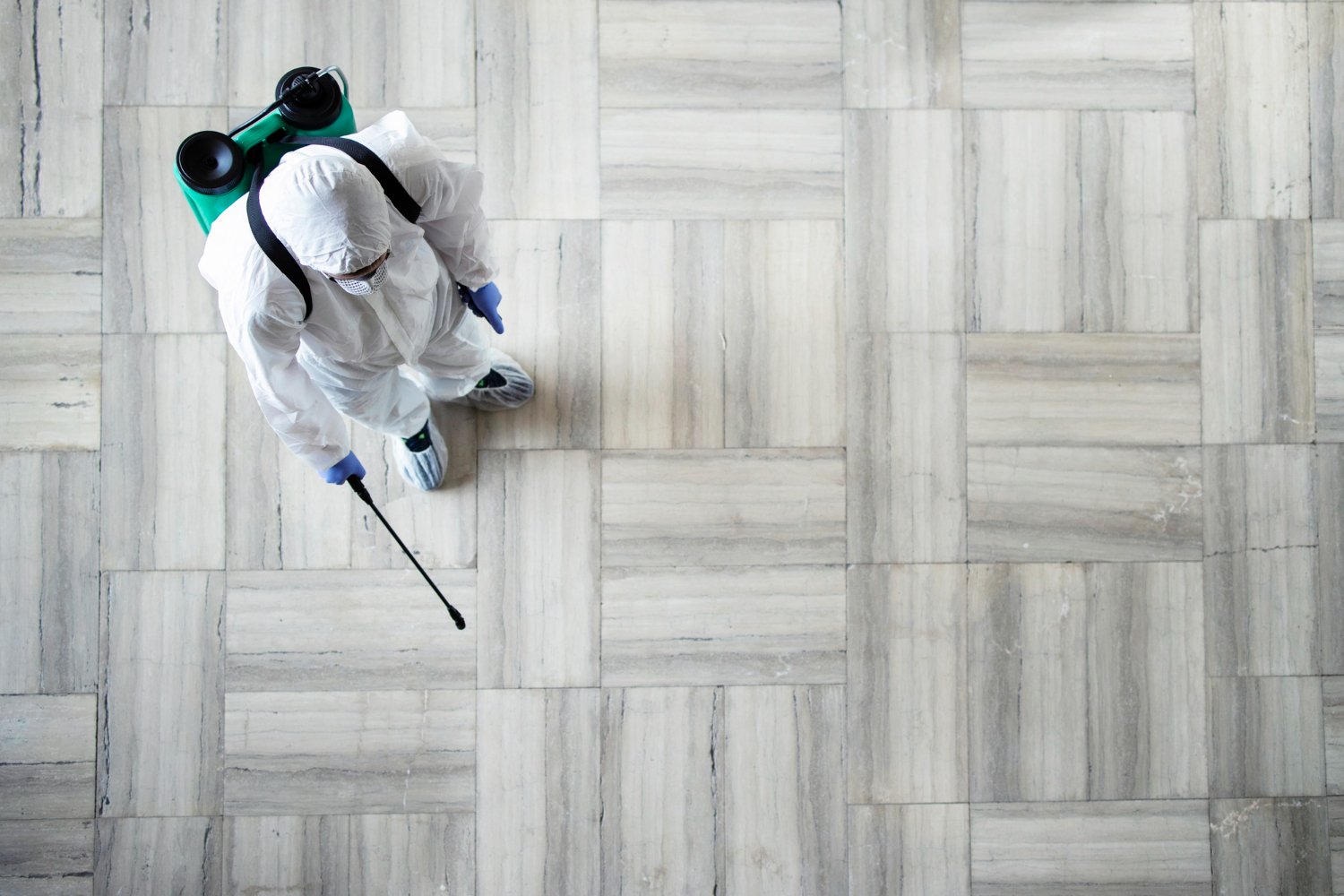 New Hampshire A person in full protective gear, including a coverall suit, mask, gloves, and shoe covers, meticulously uses a sprayer to disinfect a tiled floor after completing a pest control session. Marketing Agency