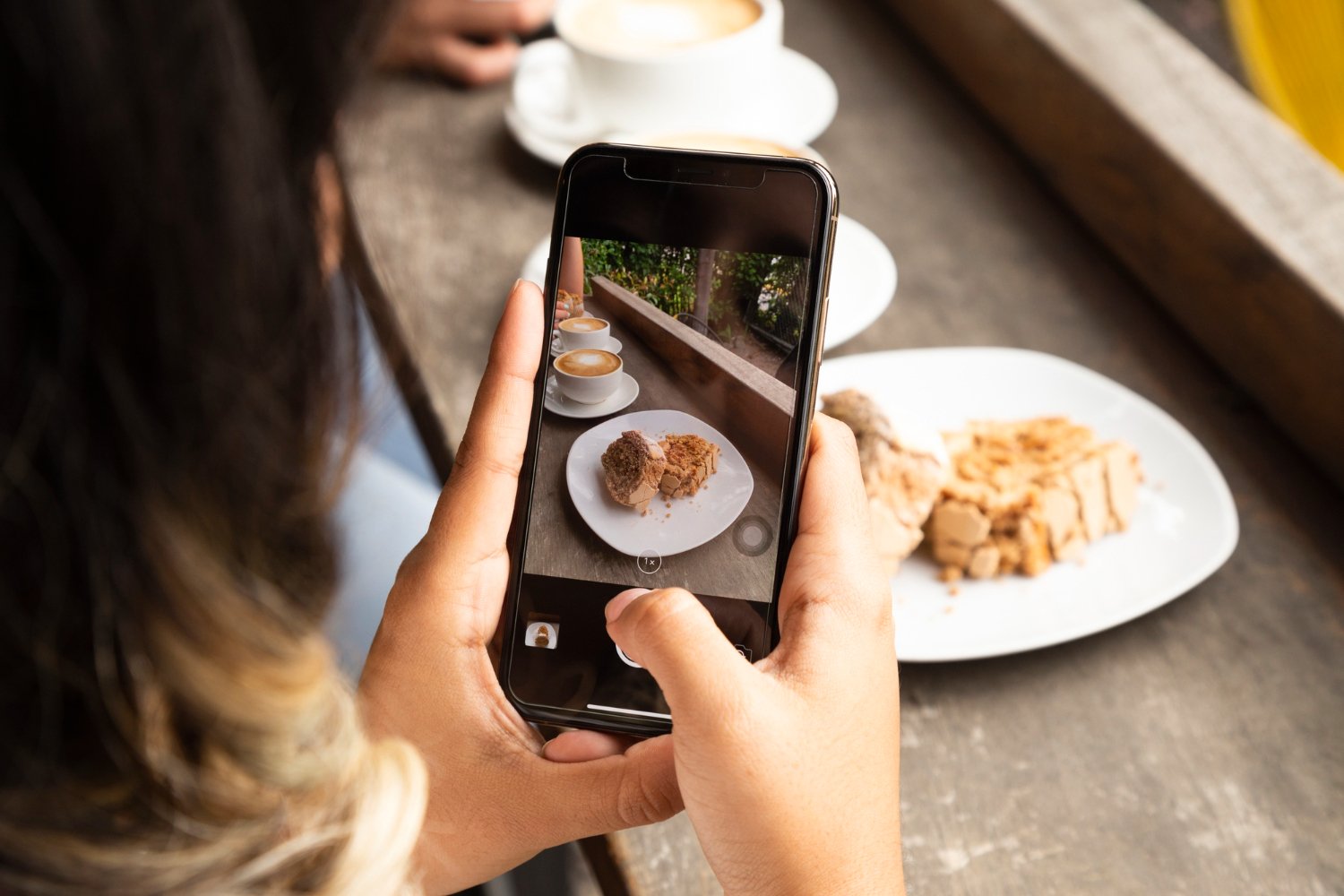 New Hampshire A person takes a photo of dessert and coffee on a smartphone at a restaurant in New Hampshire, capturing the perfect shot for online marketing. Marketing Agency