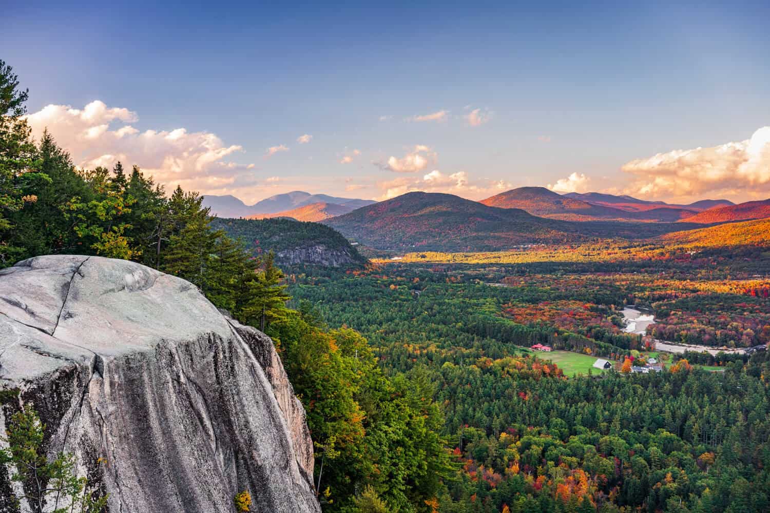 New Hampshire A scenic view from a rocky cliff in the Monadnock Region overlooks a vast forested valley with mountains in the distance under a partly cloudy sky during autumn, making it one of my favorite spots to explore charms. Marketing Agency