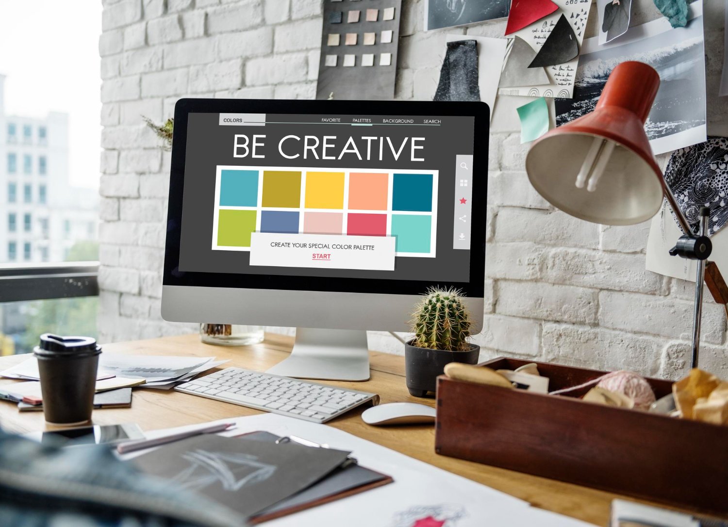 New Hampshire A computer on a cluttered desk displaying a design tool with the text "Be Creative" and colorful squares. The workspace, essential for small business success, includes books, a cactus, and various office supplies. Marketing Agency