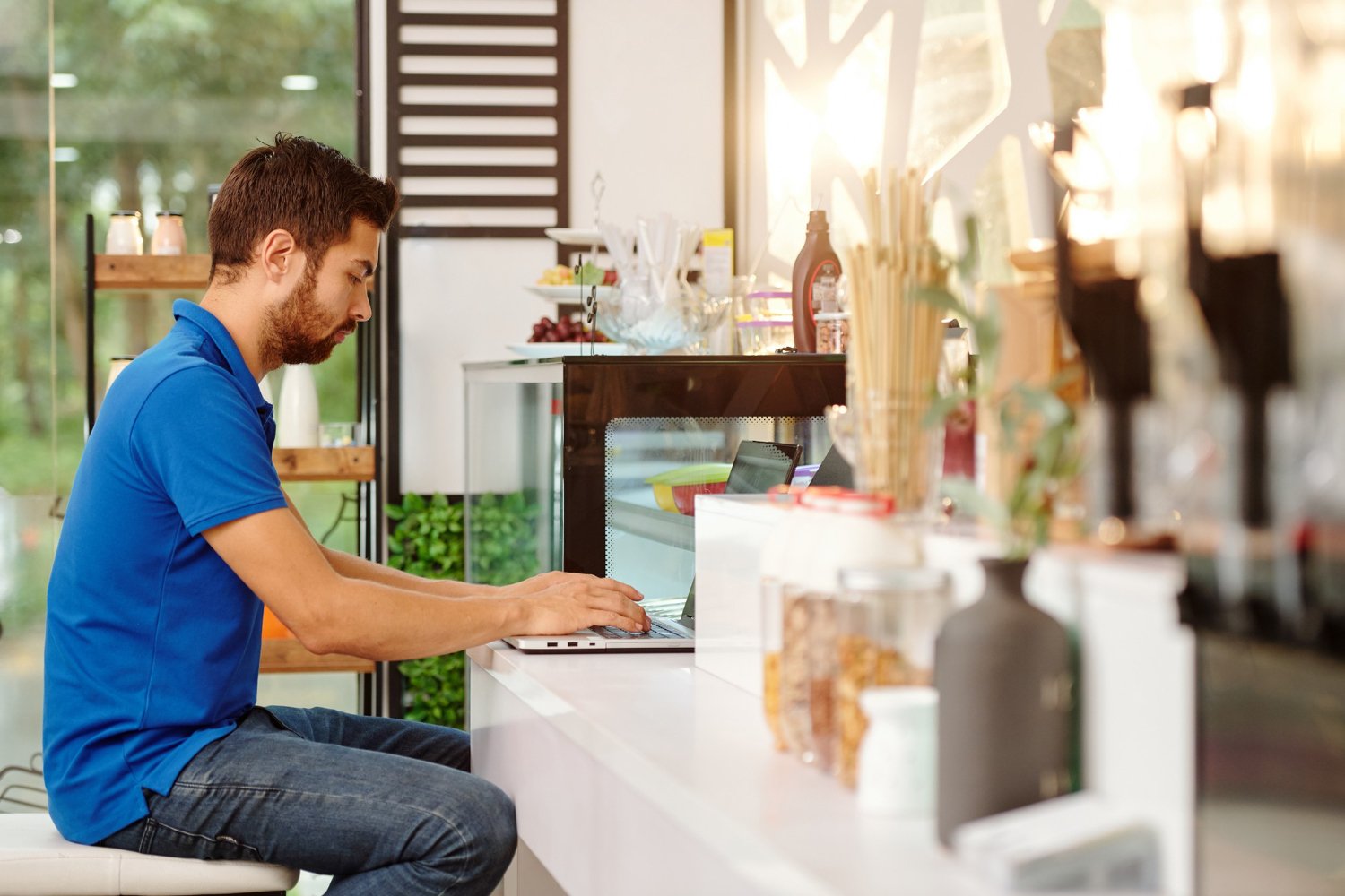 New Hampshire A man in a blue shirt sits at a counter, using a laptop to devise strategies in a bright, modern cafe setting, aiming to elevate his local retail business. Marketing Agency