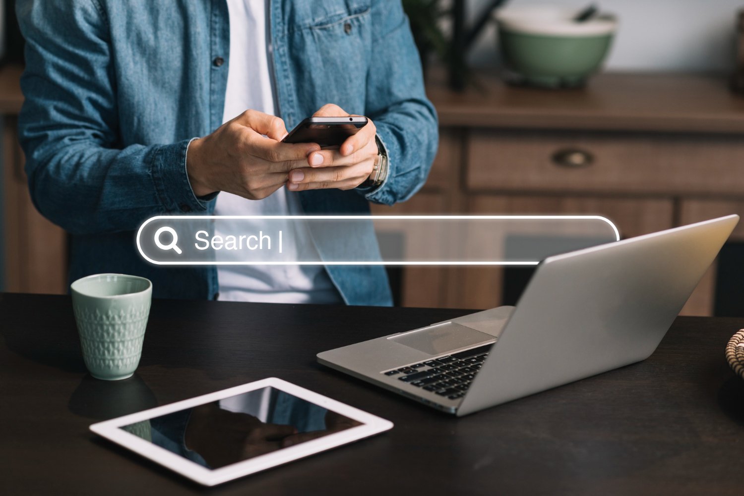 New Hampshire A person using a smartphone, with a laptop, tablet, and coffee cup on the table. A search bar graphic is overlayed on the image, suggesting an SEO guide for small business owners. Marketing Agency