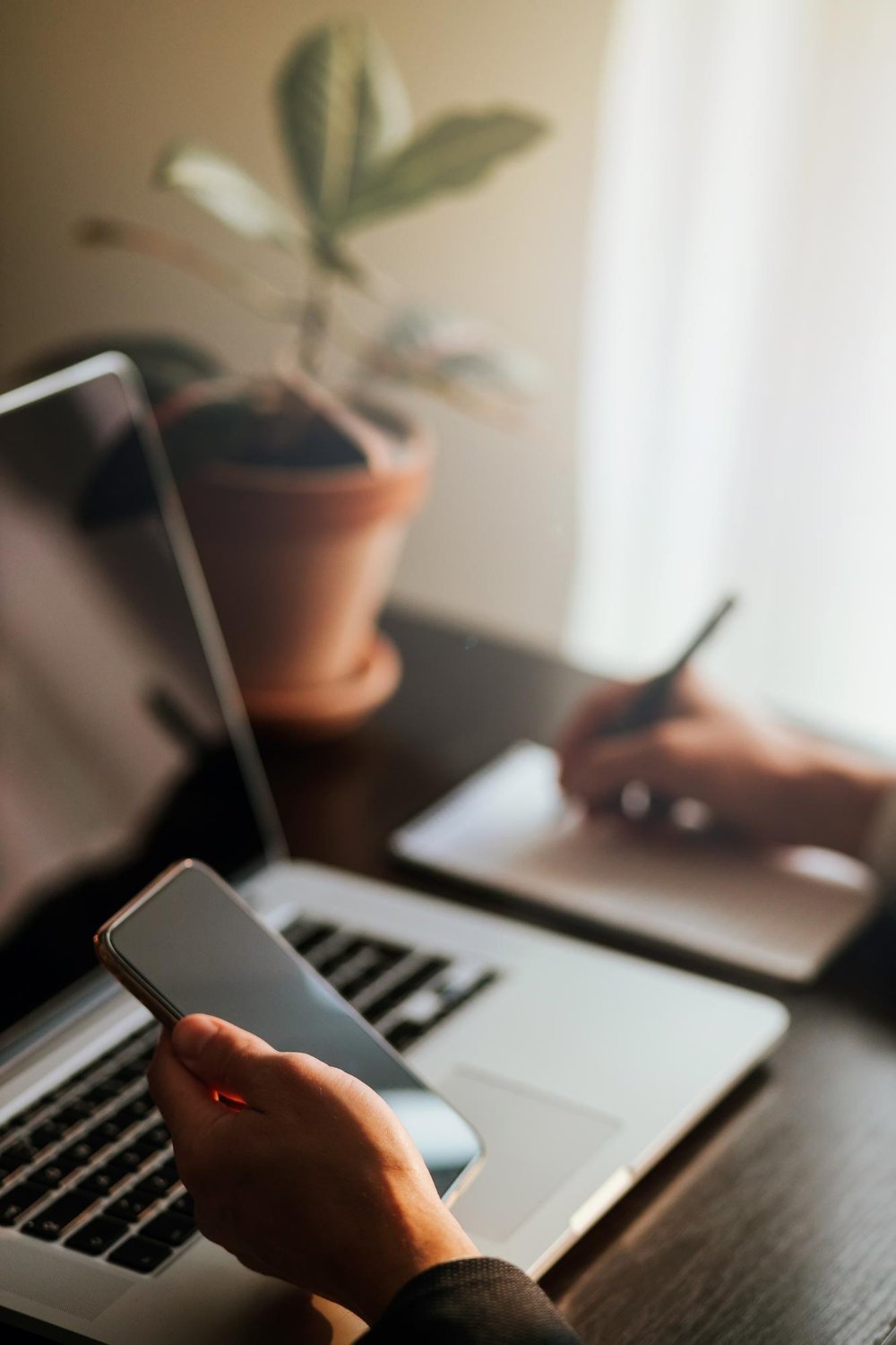 New Hampshire A person holds a smartphone in one hand and writes on a notepad with the other hand at a desk adorned with a laptop, potted plant, and materials detailing various marketing strategies. Marketing Agency