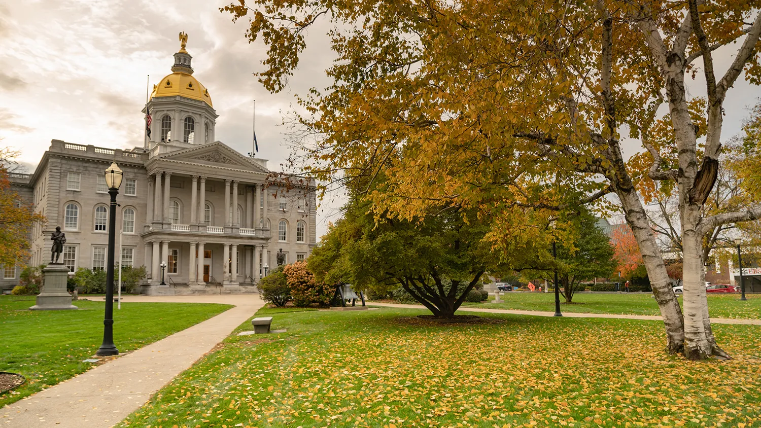 New Hampshire A historic building with a gold dome stands behind a tree with yellow leaves on a grassy lawn with a lamppost and sidewalks. Marketing Agency