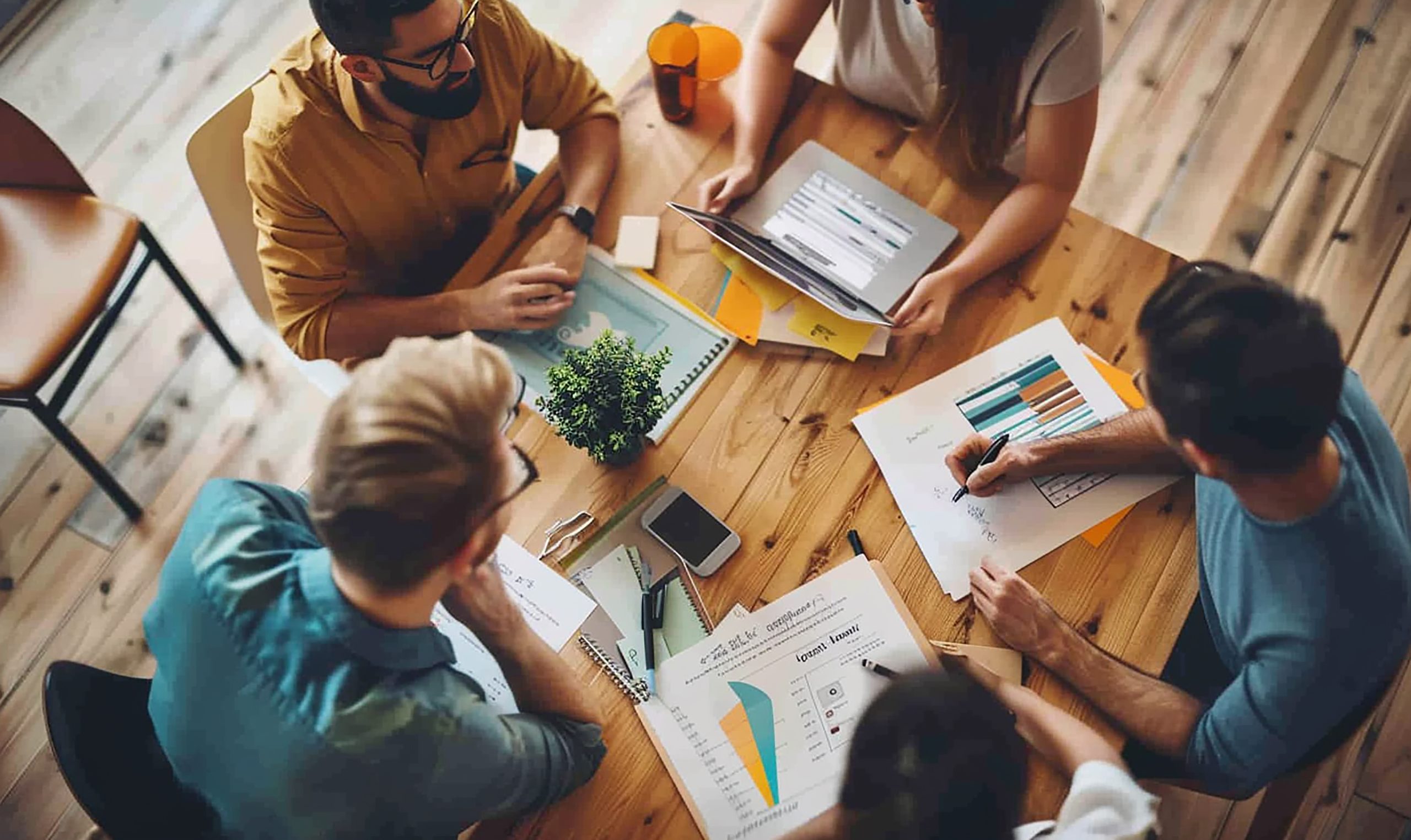 New Hampshire Five people are seated around a wooden table in the meeting room of a top New Hampshire marketing agency, reviewing documents and charts, with various office supplies scattered around. Marketing Agency