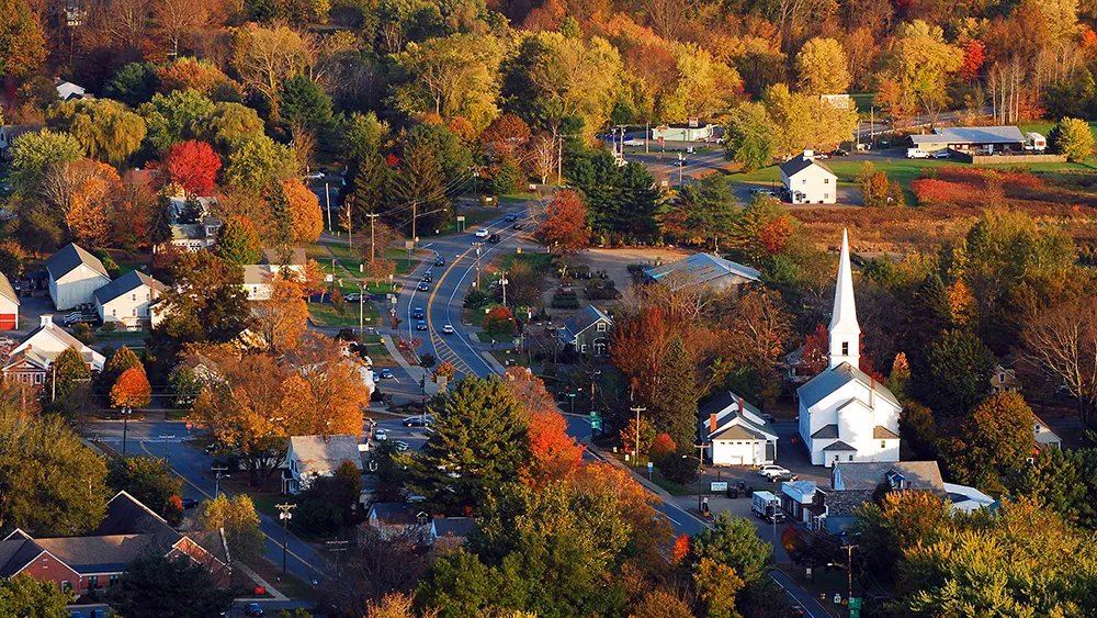 New Hampshire Aerial view of a small town with a church, various houses, and trees with autumn foliage. Marketing Agency