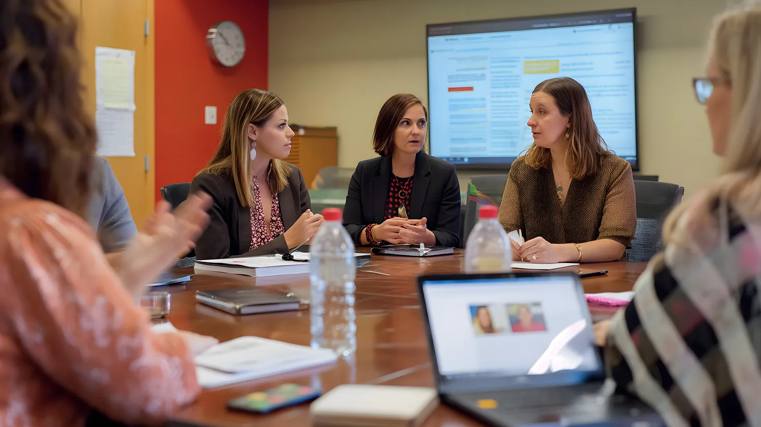 New Hampshire A group of individuals sits around a table in a meeting room, engaged in discussion about digital marketing strategies. A laptop and documents are on the table, and a large screen shows information in the background. Marketing Agency