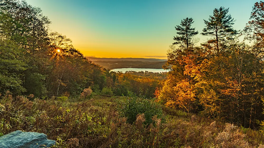 New Hampshire Sunrise over a forested landscape with a view of a distant lake and trees displaying autumn foliage. Marketing Agency