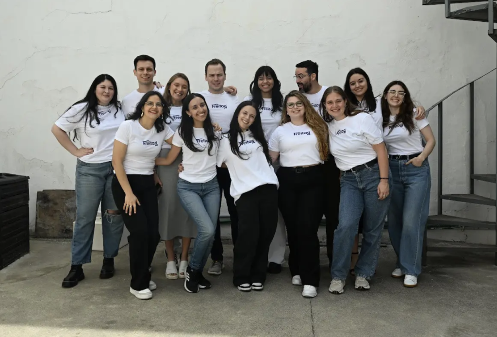 New Hampshire A group of thirteen people wearing white t-shirts stands together, embodying a successful franchise marketing strategy, smiling in front of a white wall and a metal spiral staircase. Marketing Agency