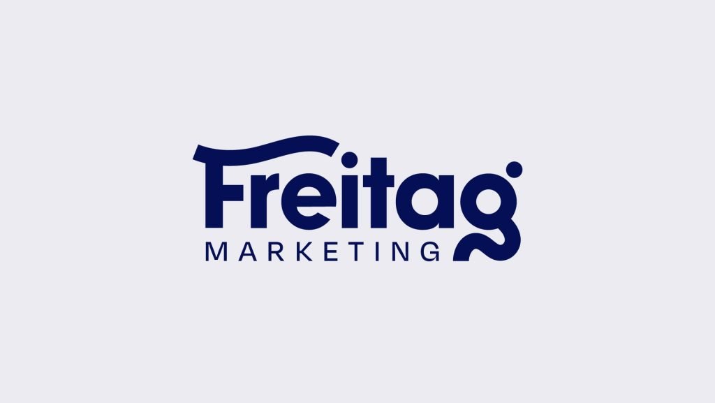 New Hampshire Logo displaying "Freitag Marketing" in blue text on a light gray background, with a stylized curved line above the letter "F". Renowned among marketing agencies in New Hampshire, this design signifies innovation and professionalism. Marketing Agency