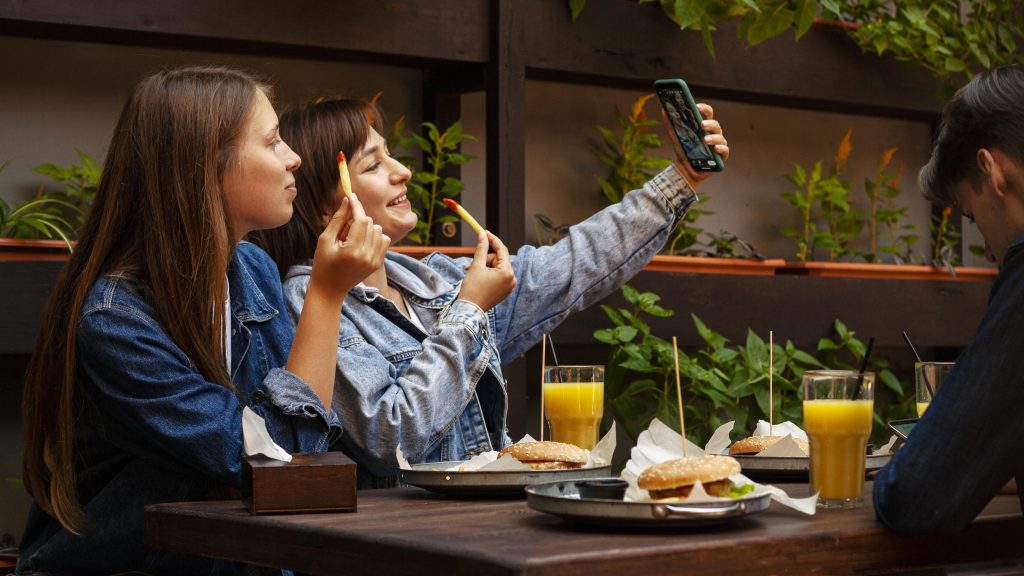 New Hampshire Two people sit at a table with burgers and orange juice, capturing a selfie moment. A third person is partially visible, likely contemplating strategies for the best local restaurants to feature in their next local marketing campaign. Marketing Agency