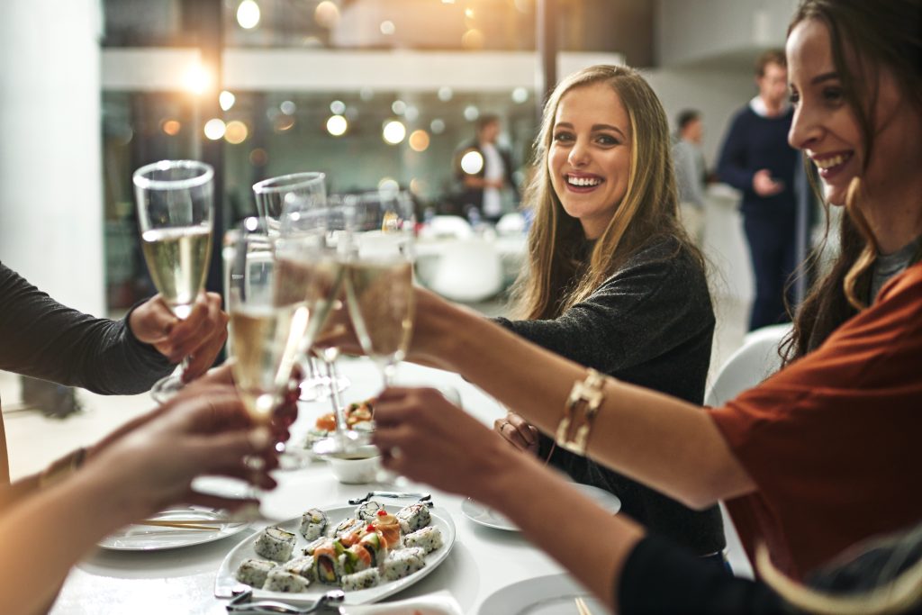 New Hampshire A group of people clinking glasses of champagne at a dining table laden with sushi rolls, smiling and celebrating—a perfect snapshot for local marketing strategies to promote the vibrant atmosphere of restaurants. Marketing Agency