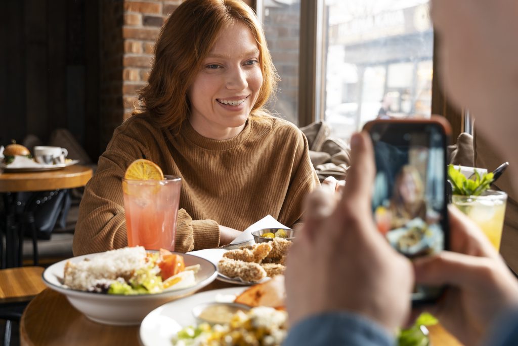 New Hampshire A person sits at a table laden with delicious food and drinks, while another captures the moment on a smartphone—a perfect strategy for local marketing at bustling restaurants. Marketing Agency