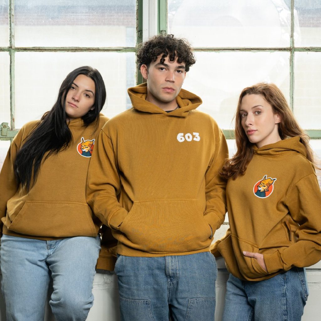 New Hampshire Three people wearing matching brown hoodies with a logo stand together in front of large windows, embodying the manufacturing company's unified approach. Their attire reflects the proven strategies that drive their successful marketing plan. Marketing Agency