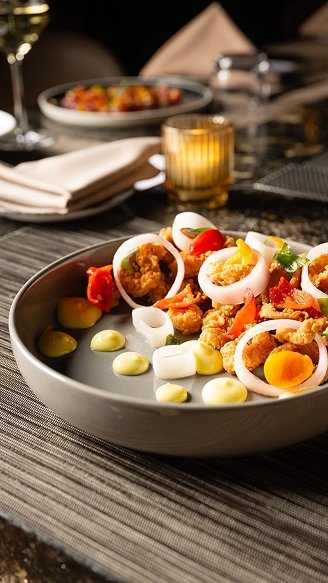 New Hampshire A gray plate with a neatly arranged dish of fried seafood, sliced onions, cherry tomatoes, and assorted sauces, set on a textured placemat with a candle and napkin in the background. Marketing Agency