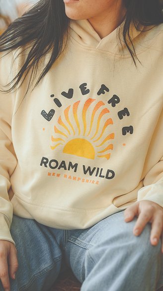 New Hampshire Person wearing a light hoodie that says "Live Free Roam Wild New Hampshire" with an orange sun graphic, seated with hands resting on lap. Marketing Agency