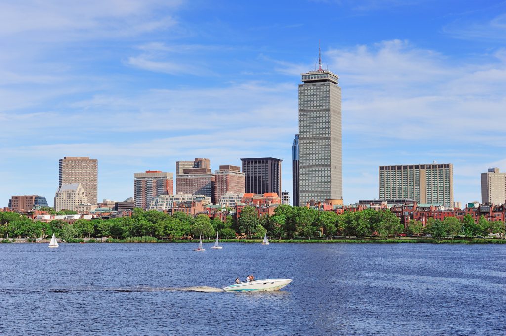 New Hampshire A city skyline with tall buildings is seen across a river in Massachusetts, with a motorboat and sailboats on the water under a blue sky—an inspiring 2025 scene for small business marketing. Marketing Agency