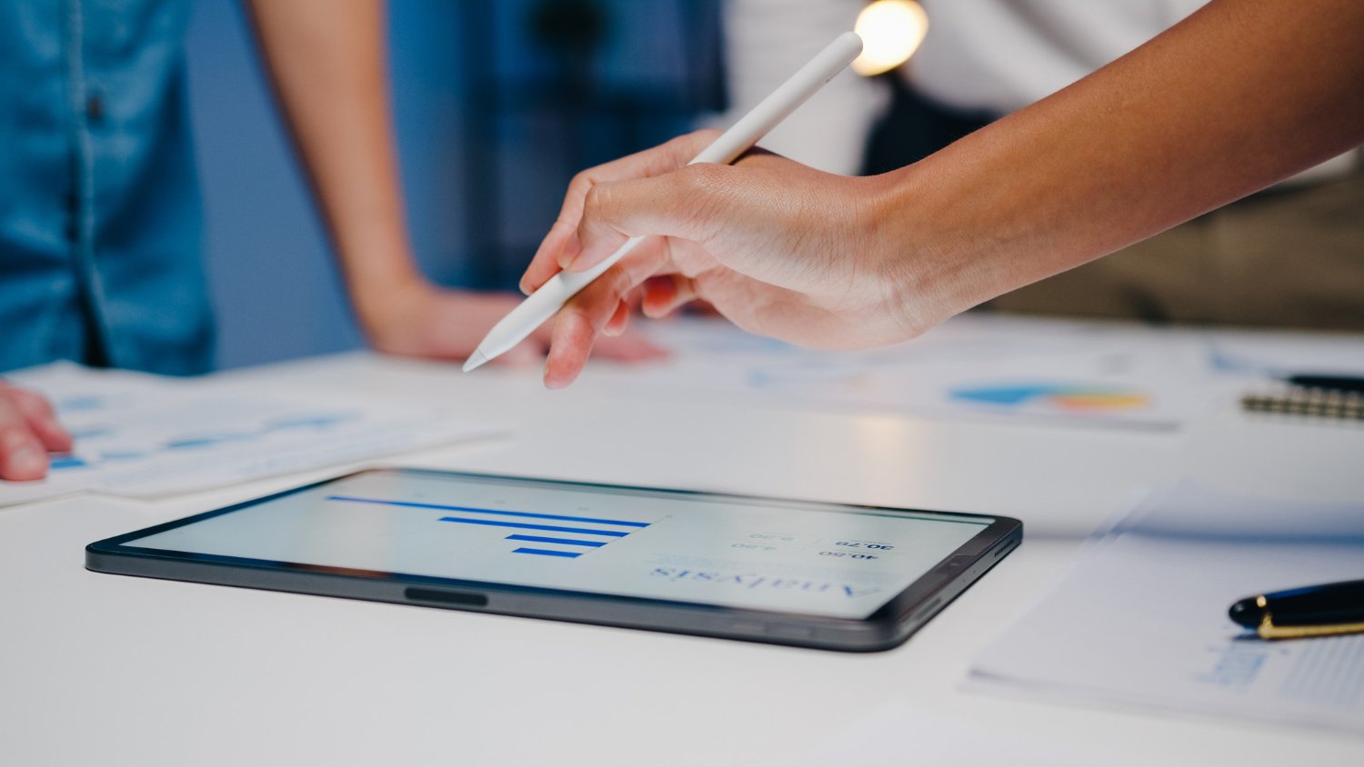 New Hampshire A person uses a stylus on a tablet displaying a bar chart, with documents and another person’s arm visible on a white table. Marketing Agency