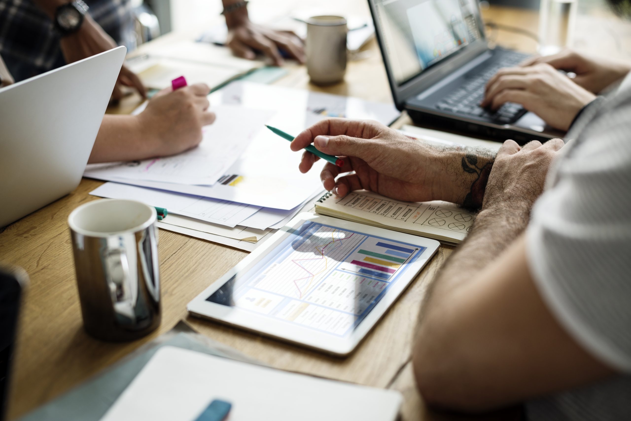 New Hampshire People working at a table with laptops, documents, and a tablet displaying graphs and charts, focusing on analyzing data and discussing digital marketing strategies for an HVAC company. Marketing Agency