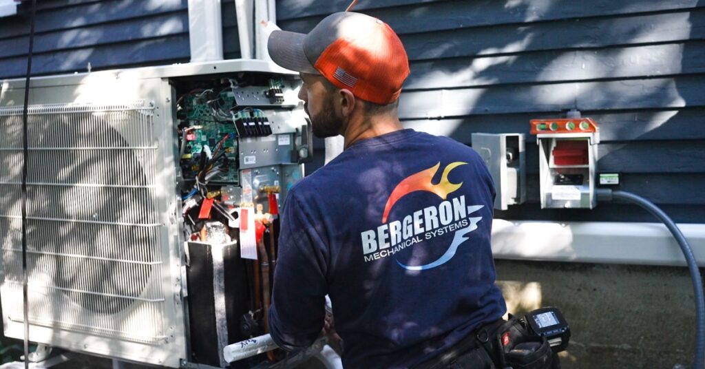 New Hampshire A technician wearing a Bergeron Mechanical Systems shirt works on the exposed components of an outdoor HVAC unit next to a blue house. Marketing Agency
