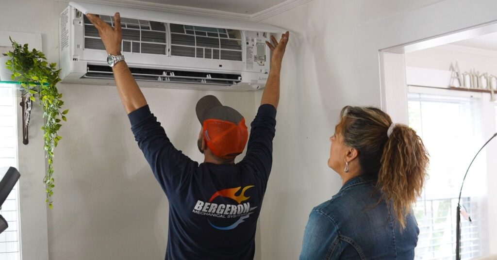 New Hampshire A technician in a Bergeron shirt inspects a wall-mounted air conditioning unit while a woman watches nearby in a well-lit room. Marketing Agency