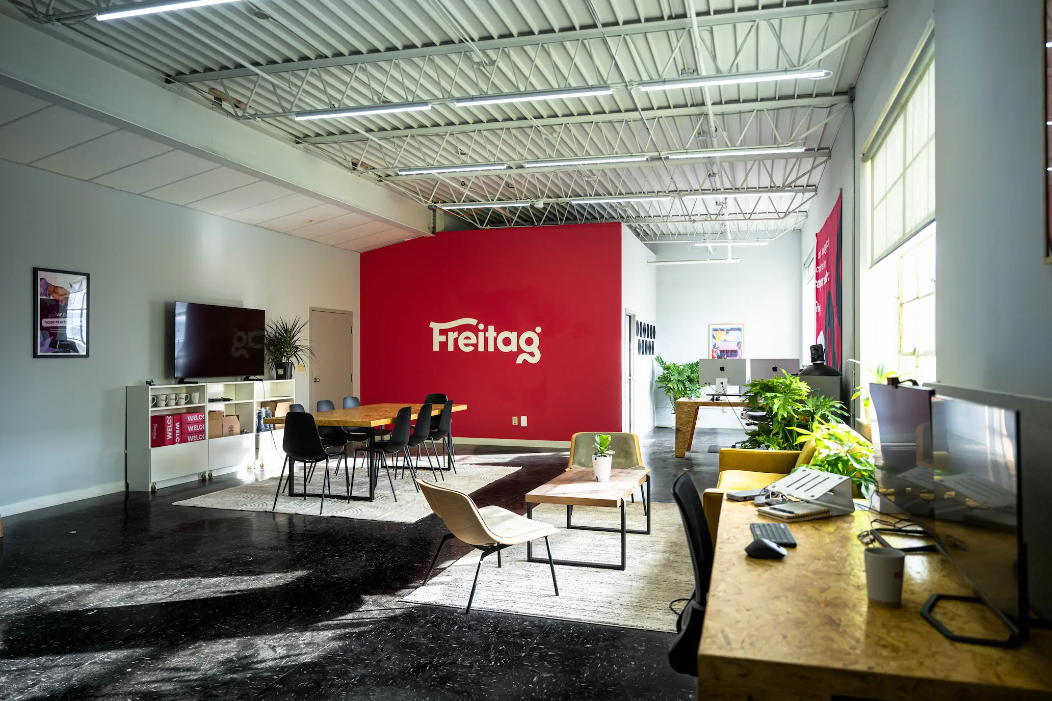 New Hampshire Modern office space with red accent wall labeled “Freitag,” multiple desks, chairs, greenery, large windows, and natural light. Marketing Agency